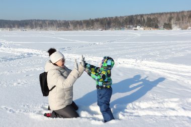 Kadın ve küçük çocuk karda oynarken bir renk ceketli