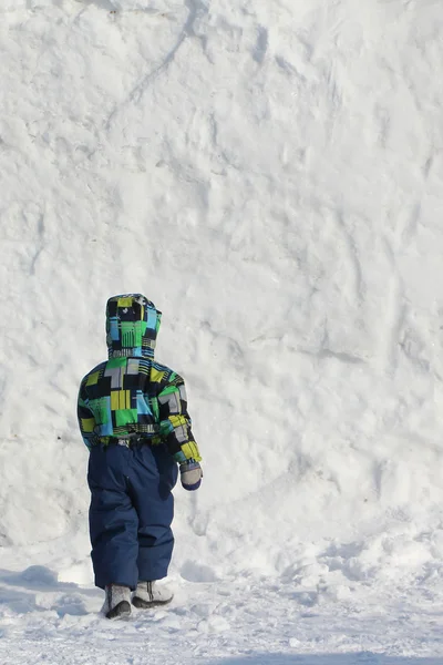 De kleine jongen in een kleur jas gonna een sneeuw-muur — Stockfoto