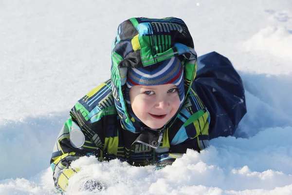 冬に雪の上に忍び寄る色のジャケットの少年 — ストック写真