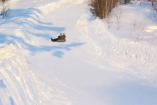 L'uomo con il bambino che cavalca un tubo di neve dalla neve — Foto Stock