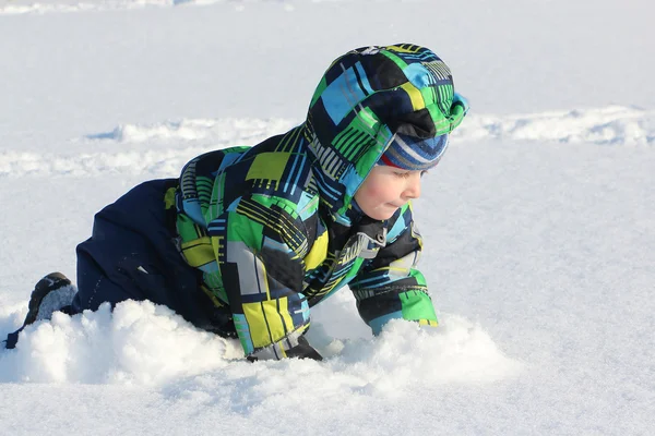 De kleine jongen in een kleur jas kruipen op sneeuw in de winter — Stockfoto