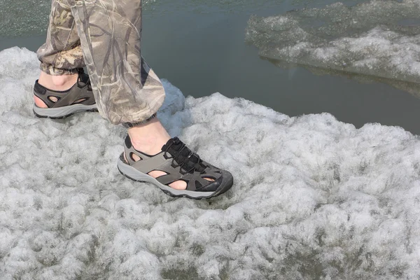 Male legs in sandals for rafting on ice of the thawing river
