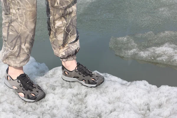 Male legs in sandals for rafting on ice of the thawing river