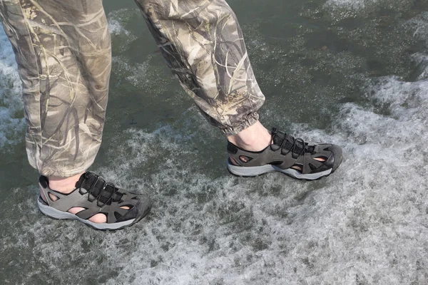 Male legs in sandals for rafting on ice of the thawing river