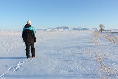 Dağlar ve mavi gökyüzü karşı bir kar alanı giden adam