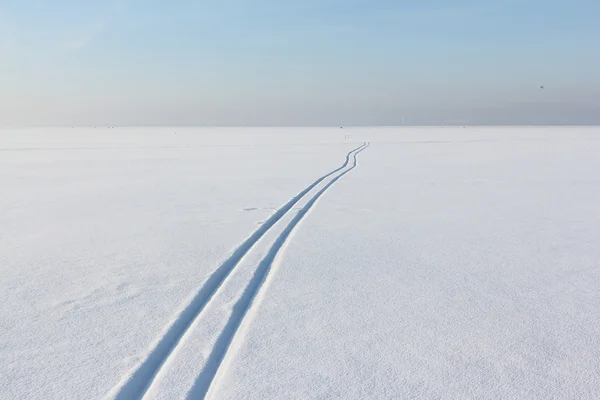 Dos pistas de esquí que salen de lejos en un campo de nieve al atardecer —  Fotos de Stock