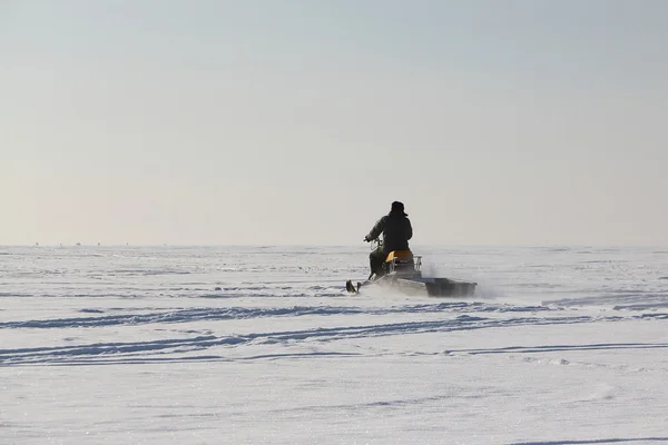 De persoon gaat op een sneeuwscooter op de bevroren rivier in de wint — Stockfoto