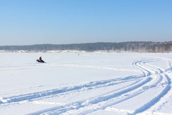 De persoon gaat op een sneeuwscooter op de bevroren rivier — Stockfoto