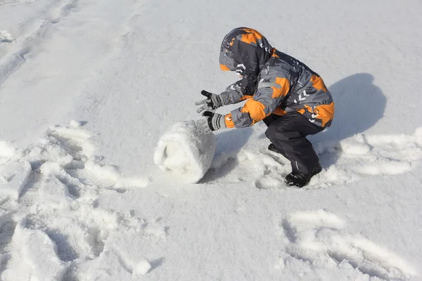 Den lilla pojken i en färg jacka med huva rullande en snöboll — Stockfoto