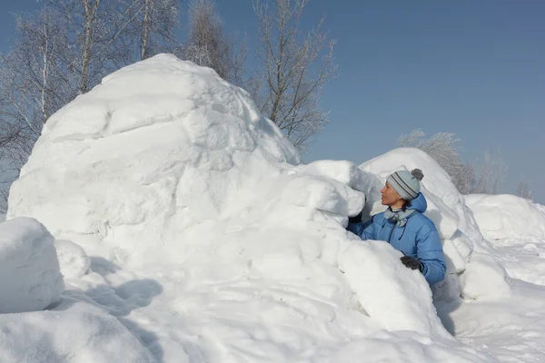 La mujer con una chaqueta azul construyendo un iglú en un claro de nieve — Foto de Stock