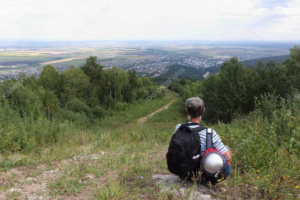 Man with a backpack sitting by the trail on Mount Tserkovka, Belokurikha city, Altai, Russia
