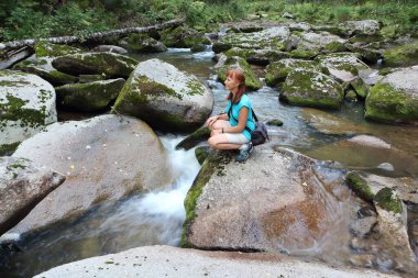 Yazın nehir kenarındaki bir taşın üzerinde oturan mutlu, kızıl saçlı kadın Belokurikha Nehri, Belokurikha Şehri, Altai Dağları, Rusya