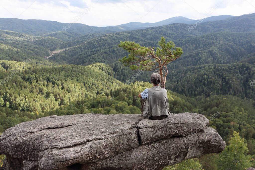 Man sitting on a rock near a lonely pine tree, Altai mountains, Belokurikha city, Russia