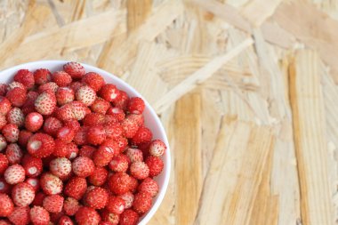Açık havada ahşap bir masa üzerinde bir tabak içinde olgun kırmızı yabani çilek