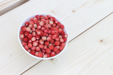 Açık havada ahşap bir masa üzerinde bir tabak içinde olgun kırmızı yabani çilek