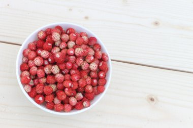 Açık havada ahşap bir masa üzerinde bir tabak içinde olgun kırmızı yabani çilek