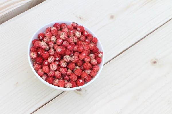 Açık havada ahşap bir masa üzerinde bir tabak içinde olgun kırmızı yabani çilek