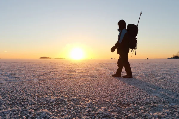 El hombre con una mochila en hielo en el río al atardecer en t —  Fotos de Stock