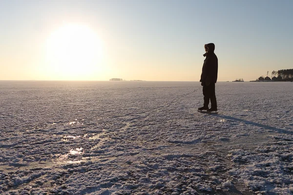 Mannen skridskor på den frusna floden på vintern vid solnedgången — Stockfoto