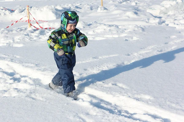 Das Kind in der farbigen Jacke, das im Winter auf Schnee läuft — Stockfoto