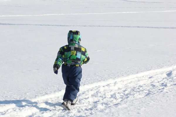 Das Kind in der farbigen Jacke, das im Winter auf Schnee läuft — Stockfoto