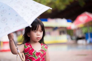 Şipşak çekim. Yağmur mevsiminde yağmurlu bir günde şemsiyeyle yürüyen tatlı bir kız. Küçük Asyalı çocuk beyaz bir şemsiye tutuyor. 3 yaşındaki çocuklar başlarının çaresine bakarlar..