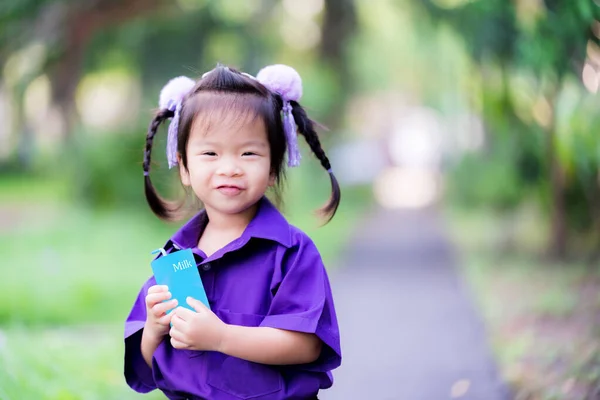 紫のドレスの女の子は青いミルクカートンまたはジュースボックスを保持立っている かわいい子供の甘い笑顔 子供たちは朝に牛乳を飲む 子供は髪を紫色の弓で縛った 4歳の子供 — ストック写真