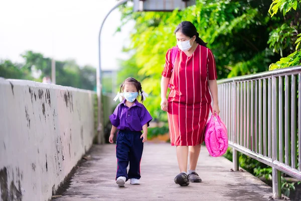 Family wear cloth masks. Mother carrying pink of daughter mattress bag went to school. Families protect against coronavirus disease and pm 2.5 by wearing masks while outside. New Normal concept.