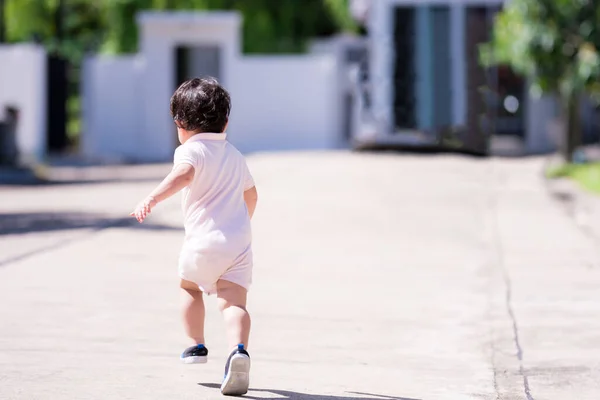 Asian boy wearing  bright Romper suit is playing on streets in front of house. Turn back to photographer. Run cheerful and bright. Concept strong child wants to leave the house from a virus outbreak.