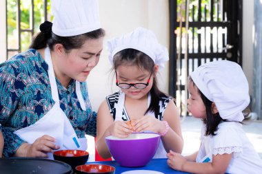 Evden öğretme konsepti. Ebeveynler yemek pişirme faaliyetleri yapan bir öğretmendir. Annem, el yapımı keklerin karışımı olarak kullanılması için torun ve kızı plastik kaseye çekiç şeklinde yumurta koymayı öneriyor..