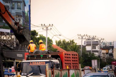 Bangkok Tayland; 09 Ekim 2019 - İki ustabaşı kamyonda durdu, sarı kasklar taktılar, uzun kollu turuncu gömlekler giydiler. İki kazıcı çalışıyor. Büyük endüstriyel makineler. İş yerinde güvenlik.