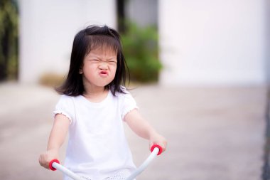 Mutlu çocuk bisiklete binerken sevimli, arsız yüzleri parlıyor. Aktif çocuklar beyaz gömlek giyiyor. Küçük kızın keyfi yerinde. Akşamları çocuk egzersizi. Asyalı kız 3 yaşında..