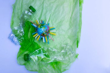 Küresel ısınma kirliliği. Mavi plastik küre, ortasındaki plastik tüp parçasıyla yerleştirildi. Dünya topu beyaz arka planda yeşil plastik torbaya konur. Yanında temiz plastik su şişesi var..
