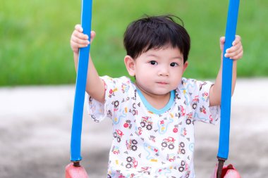 Çocuk salıncakta oynuyordu. Çocuklar salıncağın iplerine tutunmak için iki elini kullanır. Kameraya bakan sevimli bir çocuk. Anaokullarının eğlence aktiviteleri. Asyalı çocuk 2 yaşında..
