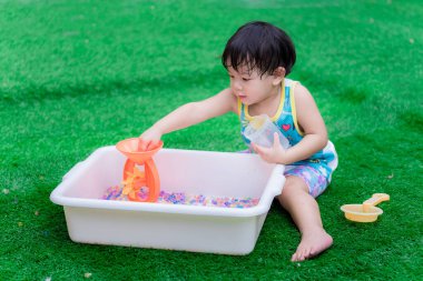 2 yaşındaki çocuk beyaz leğende renkli su boncukları oynuyor. Çocuk, pervaneleri döndürmek için turuncu su tekerleğindeki gökkuşağı boncuklarını alıyor. Duyusal öğrenme ve uygulama kavramı.