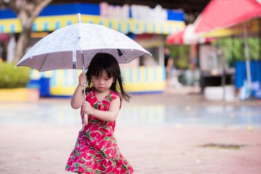 Yağmur mevsiminde, yağmurlu bir günde, üzerinde karpuz izleri olan kırmızı bir elbise giyen sevimli küçük bir kız şemsiye yürür. Çocuklar çok dikkatli yürürler. Asyalı çocuk 3 yaşında..