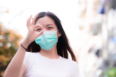 Sembol olarak el yapımı Asyalı genç kadınlar. Ve işaret ve başparmağın parmaklarına bak. Yeşil tıbbi maskenin altında, kadın tatlı tatlı gülümsedi. Çalışan kadınların insanları teşvik etmesi kavramı