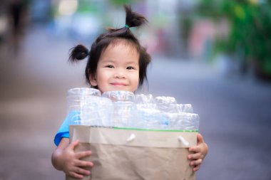 Çevreyi kurtarmak için sevgi kavramı. Küçük kız tatlı tatlı gülümsedi. Çocuklar plastik su şişelerini toplayıp satılık ve geri dönüşüm için evlerinde ayırıyorlar. Cep harçlığı kazanmak için. Yeniden Kullan.
