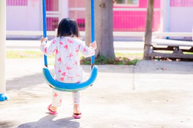 Çocuklar parkta mavi salıncakta oturuyorlar. Arkadan çocuğun resimlerini çekiyorlar. Mutlu bir şekilde sallanıyordu. Beyaz pijama giyen bir çocuk. Sabah uyandıktan sonra. Asyalı kız 3 yaşında.