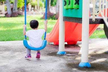 Asyalı küçük çocuğun arka tarafı yavaşça salıncakta oturuyor. Kış öğleden sonraları içiniz rahat olur. Çocuk oyun parkında rahatlamak için oyun oynuyor. 2 yaşında beyaz gömlek giyen bir bebek..