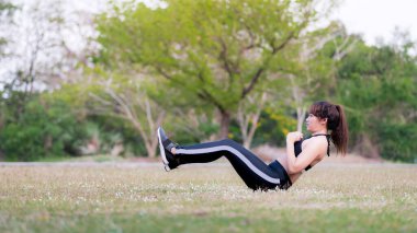 Vücut ve zihinsel gelişim arasındaki sağlıklı yaşam ve doğal denge kavramı. Parktaki yeşil çimlerde yoga antrenmanı yapan genç bir kadın. Karın kaslarını çalıştır. Karın kasılmaları.