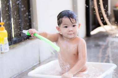 Banyo ve rahatlama kavramları. Tatlı Asyalı çocuk beyaz bir havuzda oturdu. Çocuk banyo yapıyor ve beyaz sabun oynuyor. Çocuğun elinde yeşil bir oyuncak var. Çocuklar gülümsemek eğlenceli ve parlaktır. Bebek 2 yaşında.