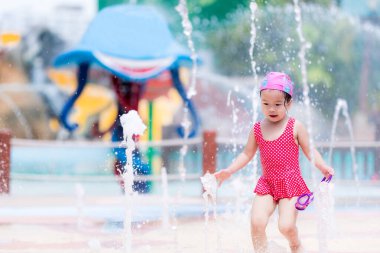 Asyalı kız çeşmenin ortasındaki bir derede heyecanlı ve mutlu. Sevimli çocuk 3 yaşında koşuyor, ıslak oynuyor ve eğleniyor. Yaz aylarında ya da sıcak havalarda şehirde aile aktiviteleri.