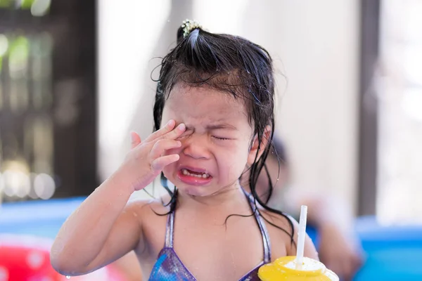 An Asian little child girl is crying while getting wet. Kid cried crying when she was dripping water on her face. Concepts of preschool social coexistence. Children 3 years old.