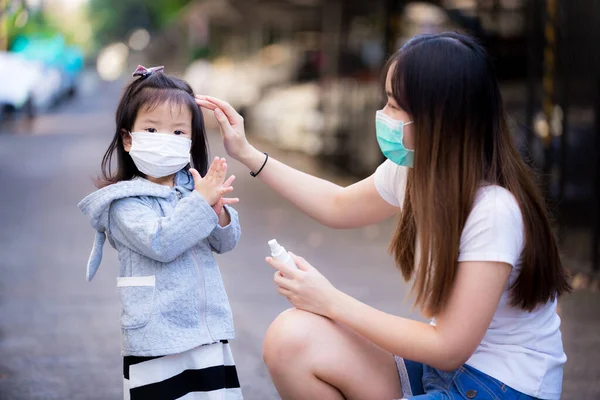 Family wear medical face masks in public places. Mother and daughter are frequently using spray alcohol to clean their hands. Families kept clean during the coronavirus disease (Covid-19) outbreak.