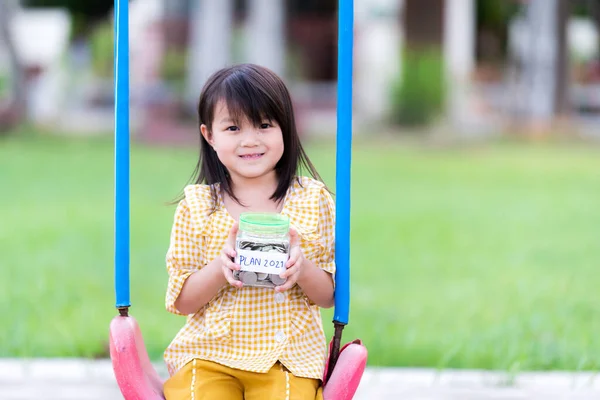 Concepts of children saving and planning for the future. Child girl smiled sweetly while holding a large coin jar of money. A white paper label reads \