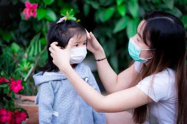 Aile, Corona virüsü salgını sırasında solunum enfeksiyonlarını önlemek için maske takıyor. Annem kızıyla maske takmak hakkında konuşuyor. Anne kızına bakar. Yeşil doğa arkaplanı.;