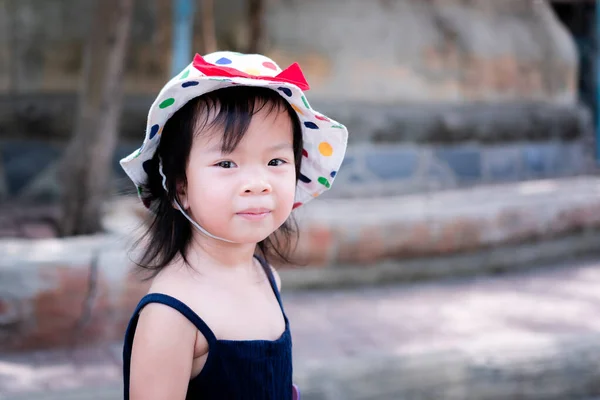 ポートレートかわいいアジアの女の子は甘い笑顔に彼女の視線を回し白い水玉の帽子を着用してください 女の子は3歳 — ストック写真