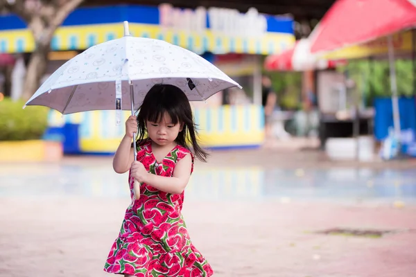 スイカのプリントの赤いドレスを着た愛らしい少女は 梅雨の日に傘を歩く 子供たちはとても注意深く歩く アジア人の子供は3歳 — ストック写真