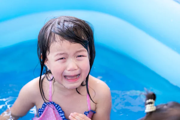 4-year-old Asian girl is crying in blue pool while playing in water and there is accident in water play activities at home. Child is crying and hurt  in an accident. Concept of child safety and sports